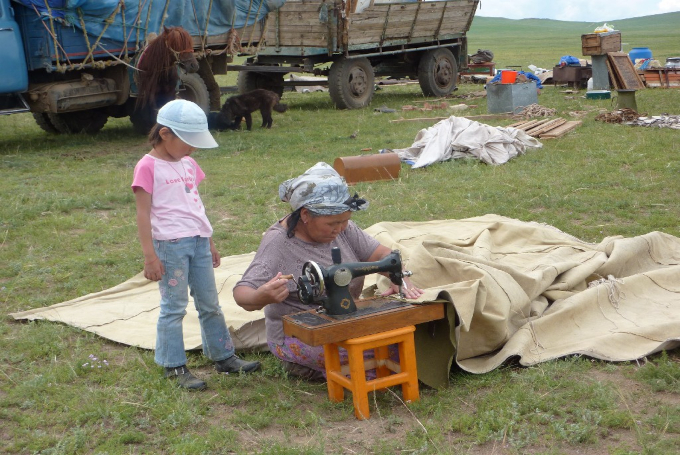 Alltag in der mongolischen Steppe mit Person an einer Nähmaschine in traditioneller Umgebung.